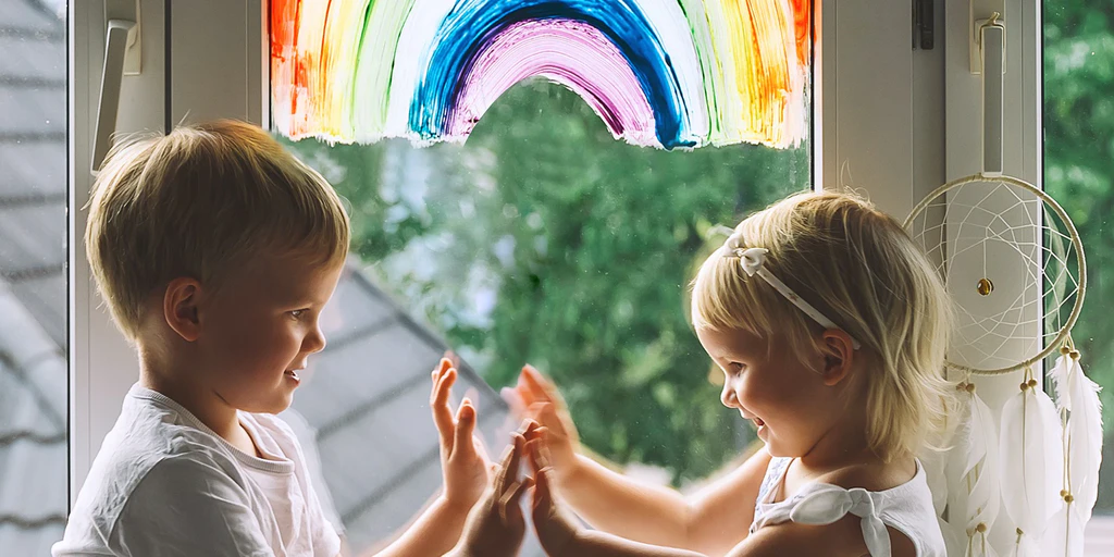 Kinder sitzen vor Fenster mit Regenbogen