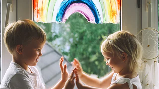 Kinder sitzen vor Fenster mit Regenbogen